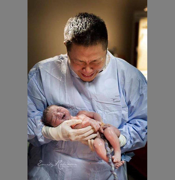 Мужчина плачет держа на руках только что родившегося малыша