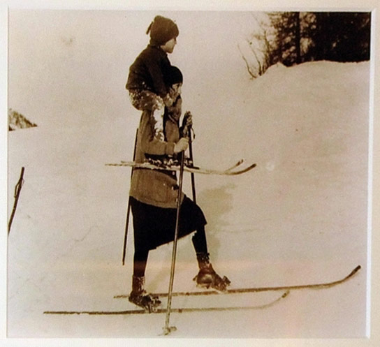Женщина на лыжах в длинной юбке, с ребенком на плечах